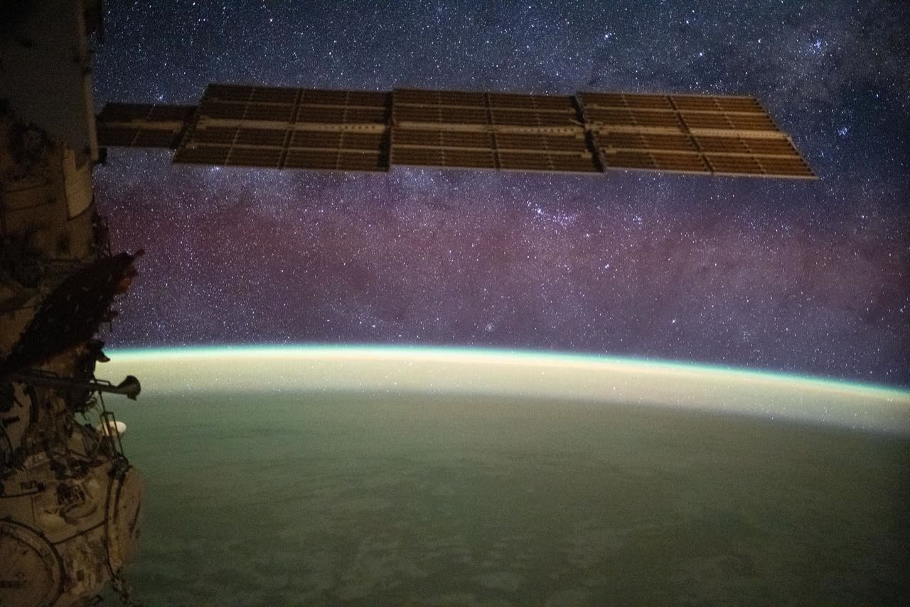 The Milky Way spans the night sky above a yellow-green airglow
